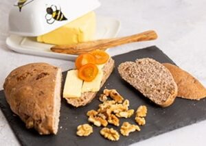 Walnut loaf on black slate sliced with a cheese and tomato topping, butter dish with butter and wooden knife and walnuts